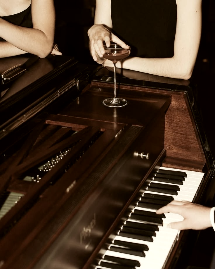 Hands on piano keys during an evening, a glass resting on the instrument