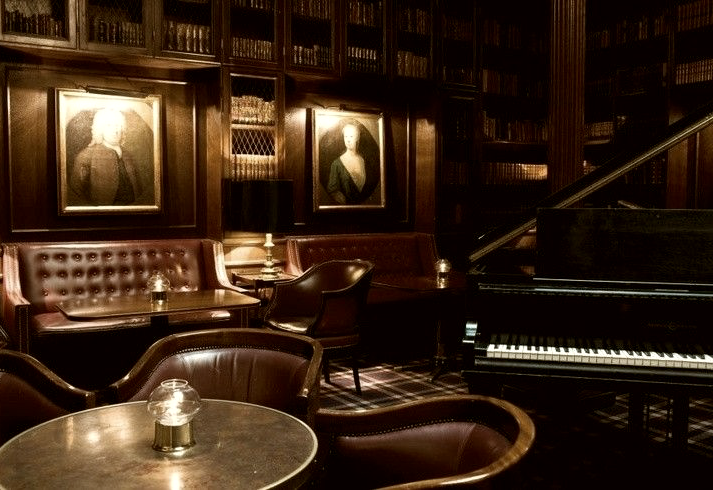 Wood-panelled bar with leather seating and a grand piano, candlelit